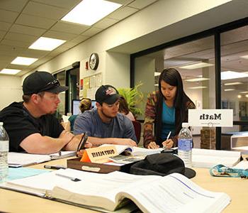 Students sitting at table with Math sign receiving help